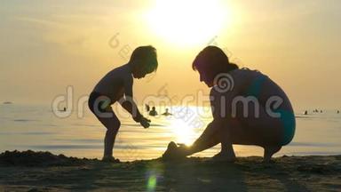 一个快乐的<strong>母亲</strong>和<strong>孩子</strong>在沙滩上玩耍的<strong>剪影</strong>。 妈妈和<strong>孩子</strong>一起建造一座沙堡